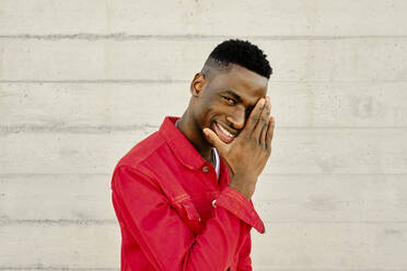 Porträt eines lächelnden jungen Mannes in roter Jacke vor einer Betonwand - AODF00226