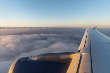 Wing of airplane flying over clouds at dawn - WPEF03865