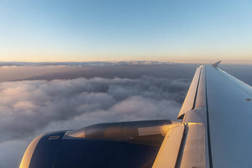 Flügel eines Flugzeugs, das in der Morgendämmerung über Wolken fliegt - WPEF03865