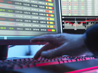 Hände eines Händlers, der auf einer Tastatur vor einem Computerbildschirm tippt, auf dem Börsendaten angezeigt werden - ABRF00823