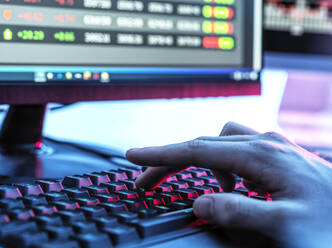 Hände eines Händlers, der auf einer Tastatur vor einem Computerbildschirm tippt, auf dem Börsendaten angezeigt werden - ABRF00825