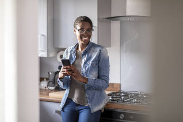 Smiling woman with smart phone in kitchen - WPEF03930