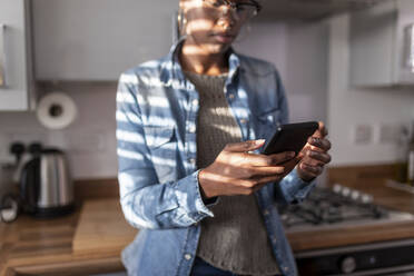 Woman looking at smart phone in kitchen - WPEF03933