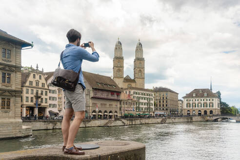 Switzerland, Zurich, Man photographing Limmat river and old town buildings - TAMF02737