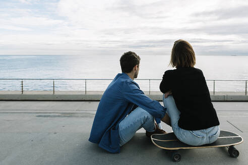 Paar auf dem Boden sitzend in einem Skateboard, mit Blick auf das Meer - XLGF00971