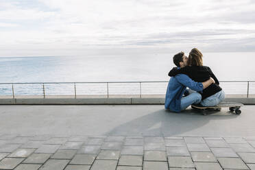Couple sitting on ground in skateboard, facing sea - XLGF00972