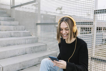 Lächelnde junge Frau beim Musikhören im Freien - XLGF00980