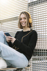 Portrait of smiling young woman listening to music outdoors - XLGF00982