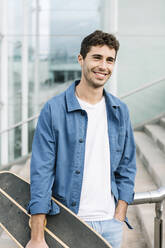 Portrait of smiling young man with skateboard outdoors - XLGF00983