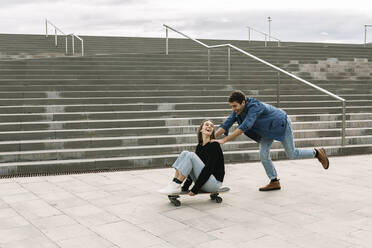 Mann schiebt Frau auf Skateboard sitzend - XLGF01000
