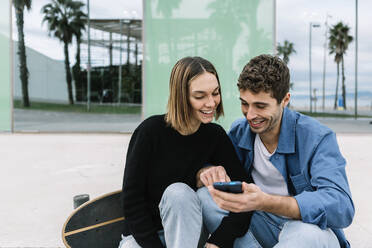 Smiling couple looking at smart phone outdoors - XLGF01005