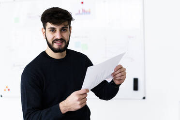 Porträt eines jungen Geschäftsmannes, der ein Dokument im Konferenzraum eines Kreativbüros hält - GIOF10532