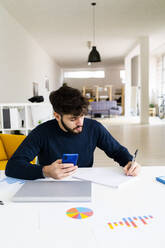 Young businessman writing at desk in creative office - GIOF10542