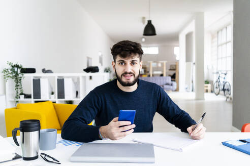 Porträt eines jungen Geschäftsmannes, der am Schreibtisch in einem kreativen Büro schreibt - GIOF10543