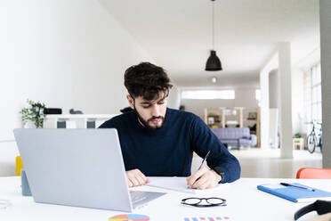Young businessman writing at desk in creative office - GIOF10544