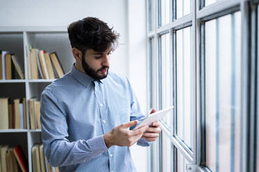 Junger Geschäftsmann benutzt digitales Tablet am Fenster in einem kreativen Büro - GIOF10555