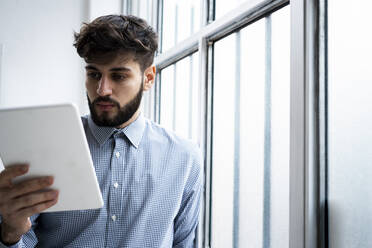 Young businessman using digital tablet by window in creative office - GIOF10556