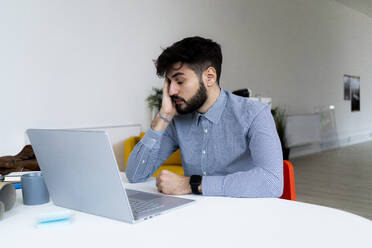 Tired businessman looking at laptop in creative office - GIOF10567