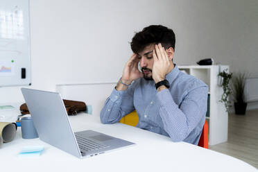 Tired businessman rubbing temples at desk in creative office - GIOF10568