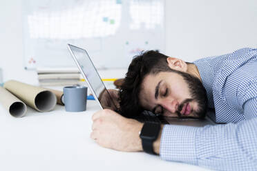Tired businessman sleeping on laptop in creative office - GIOF10569
