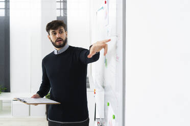 Businessman having presentation in office, pointing at whiteboard - GIOF10576