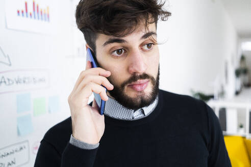 Geschäftsmann im Gespräch am Telefon vor einer Tafel im Büro - GIOF10586