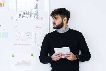 Geschäftsmann mit digitaler Tafel vor einem Whiteboard im Büro stehend - GIOF10589