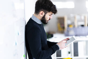 Geschäftsmann, der ein digitales Tablet vor einem Whiteboard im Büro benutzt - GIOF10592