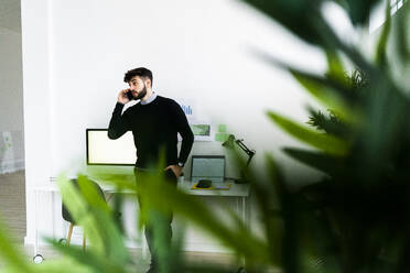 Geschäftsmann, der im Büro mit seinem Smartphone telefoniert, grüne Pflanzenblätter im Vordergrund - GIOF10601