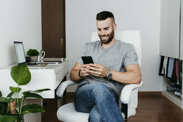 Lächelnder Mann arbeitet zu Hause an Laptop und Handy - EBBF02122