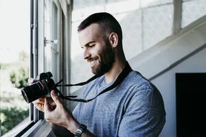 Lächelnder Mann bei der Arbeit mit der Kamera zu Hause - EBBF02129