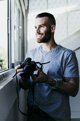 Smiling man working with camera at home - EBBF02130