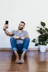 Lächelnder junger Mann nimmt Selfie zu Hause - EBBF02131