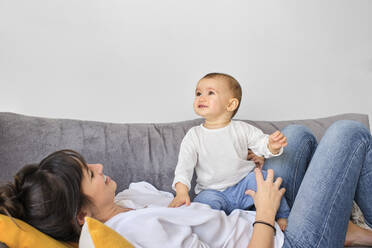 Mother playing with baby daughter on sofa - AODF00251