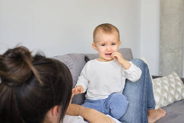 Baby girl grimacing while playing with mother on sofa - AODF00254