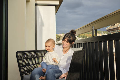 Mutter und kleine Tochter sitzen zusammen im Sessel auf dem Balkon - AODF00260
