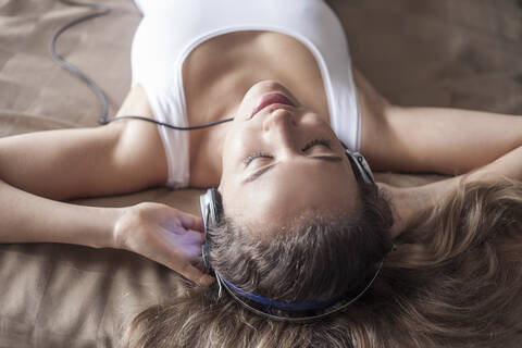 Close-up of woman listening music through headphones while relaxing on bed stock photo