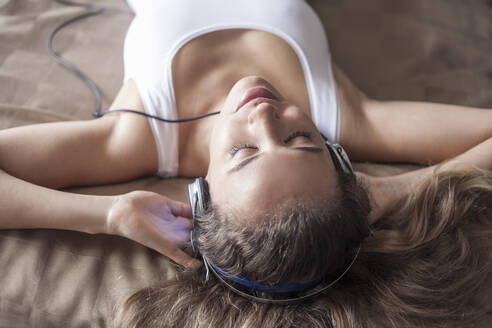 Nahaufnahme einer Frau, die beim Entspannen auf dem Bett über Kopfhörer Musik hört - AJOF00967