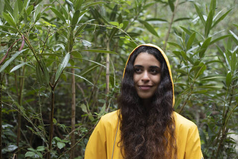 Young woman wearing yellow raincoat contemplating while standing against plants in forest stock photo