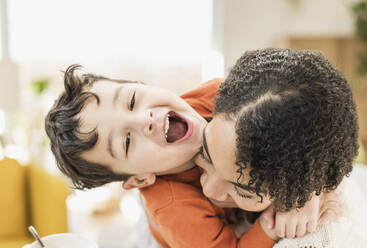 Lächelnder Junge umarmt Mutter beim Spielen zu Hause - UUF22583