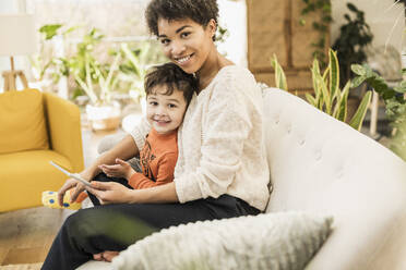 Lächelnde Mutter und Sohn mit digitalem Tablet zu Hause sitzend - UUF22595