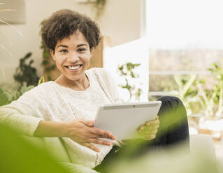 Junge Frau benutzt ein digitales Tablet, während sie zu Hause sitzt - UUF22600