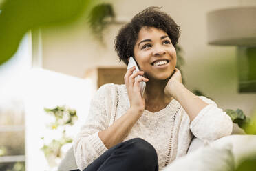 Young woman talking on mobile phone while sitting at home - UUF22613