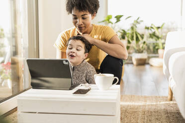 Mutter und Sohn benutzen ein digitales Tablet, während sie zu Hause sitzen - UUF22638