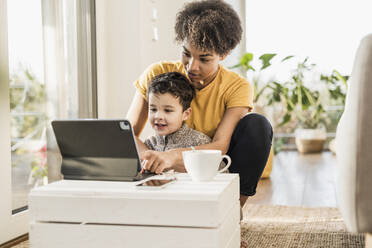 Mutter zeigt ihrem Sohn ein digitales Tablet, während sie zu Hause sitzt - UUF22639