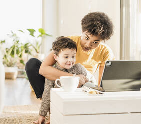 Young woman and boy using digital tablet while studying online sitting at home - UUF22640