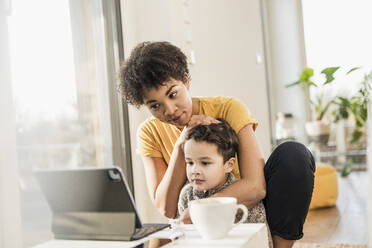 Mutter und Sohn sehen zu Hause auf einem digitalen Tablet zu - UUF22642