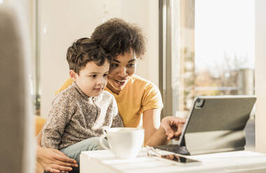 Frau unterrichtet Jungen mit Hilfe eines digitalen Tablets, während sie zu Hause sitzt - UUF22643