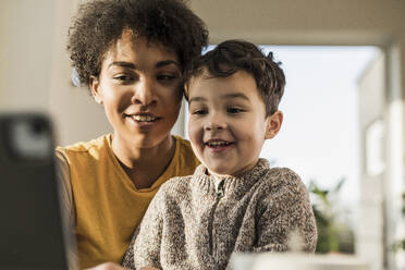Smiling woman using digital tablet while sitting with boy at home - UUF22644