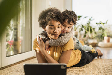 Mother and son using digital tablet while lying at home - UUF22648